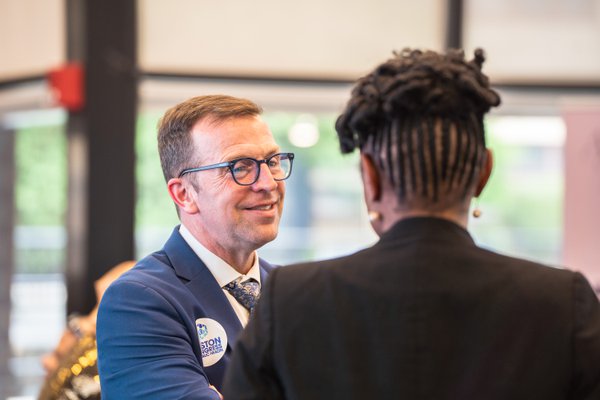 A guest in a navy blazer wearing a Boston Congress of Public Health pin shakes hands with another attendee.