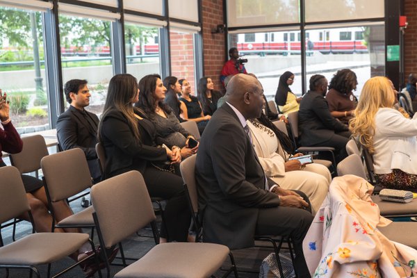 Rows of seated attendees, leaning into the program, daylight pouring in through the windows behind them.