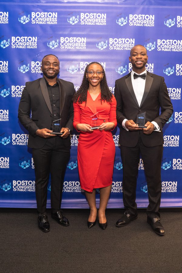 Three honorees on the BCPH backdrop: a man in a black suit on the left, a woman in a red dress in the middle, and a man in a tuxedo with bowtie on the right, all holding awards.