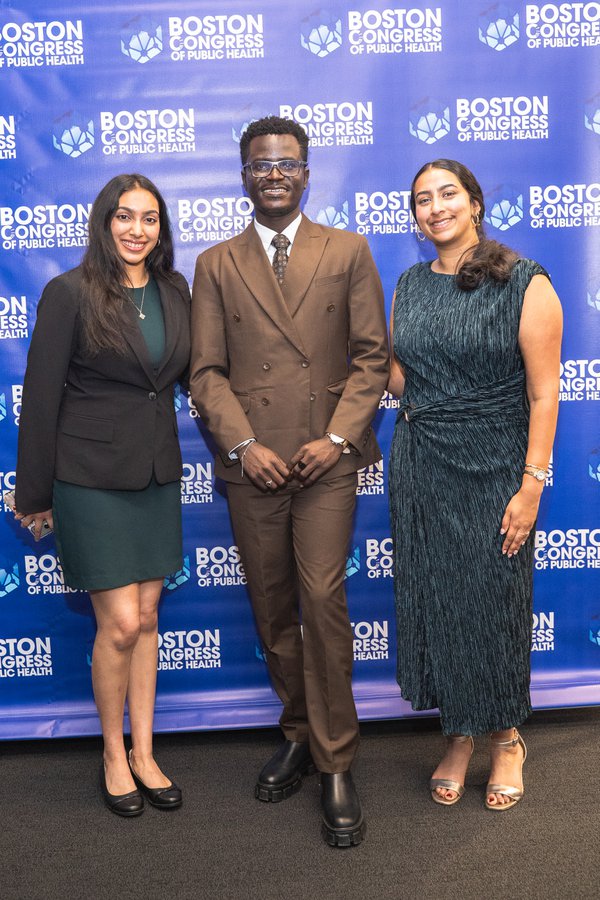 James Arthur in a brown double-breasted suit, flanked by two friends in dark dresses, posing on the BCPH backdrop.