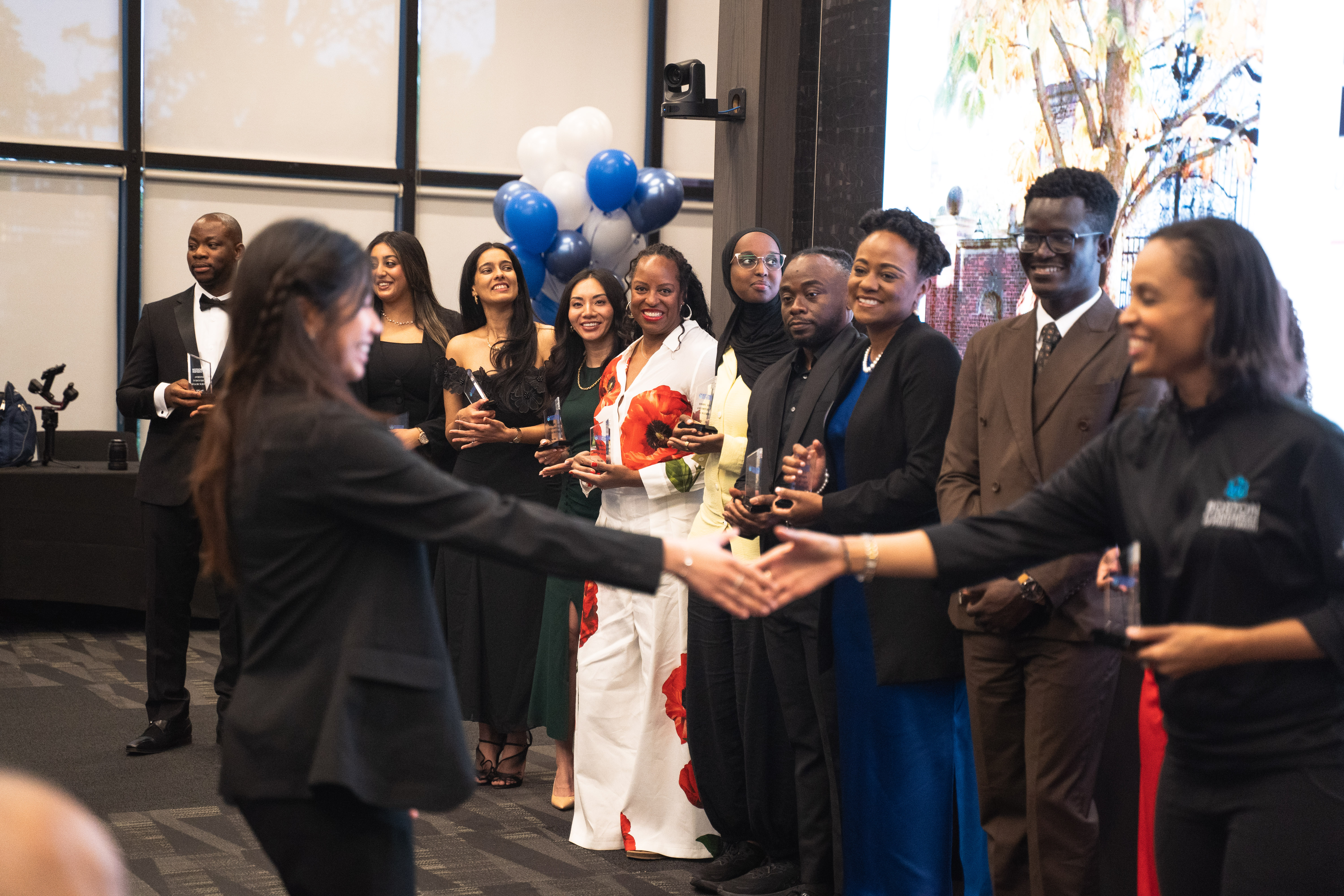 A group of 40 Under 40 honorees together with their trophies, blue and white balloons in the background.