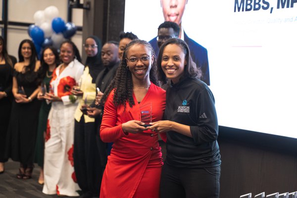 A 40 Under 40 honoree in a red dress accepts her award alongside Dr. Candice D. Carpenter in a BCPH zip top, both smiling.