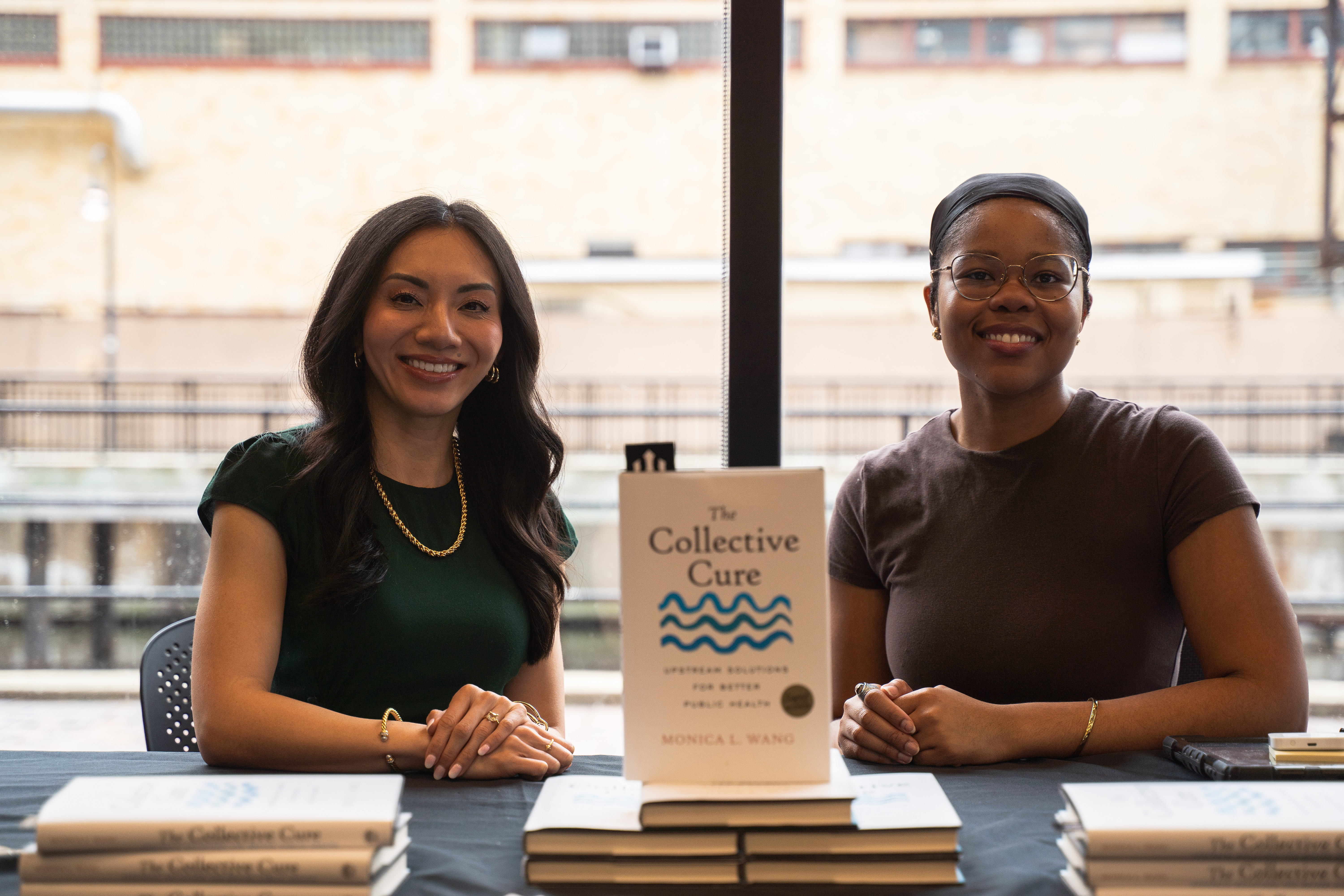 Dr. Monica L. Wang seated at the book table beside her book rep, with copies of The Collective Cure displayed in front of them.